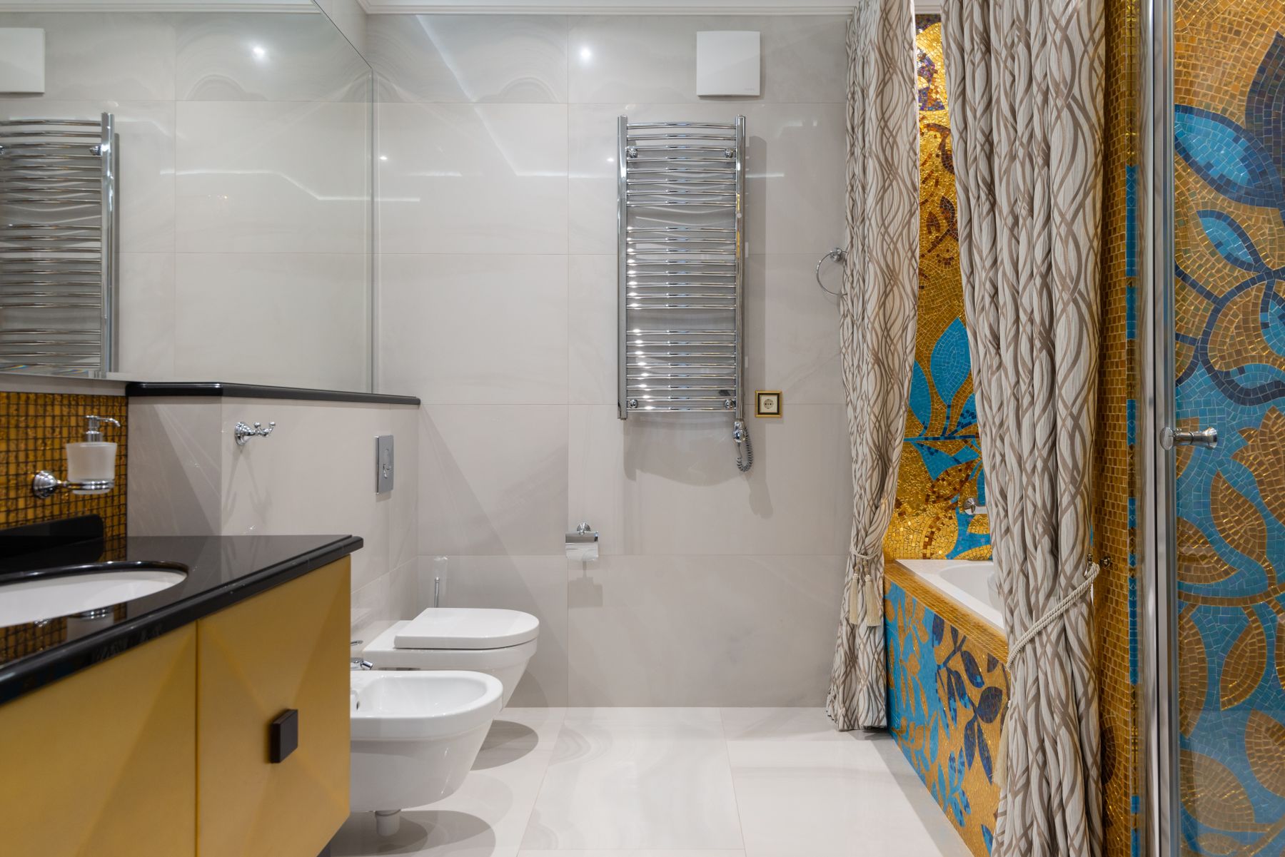 Bathroom with yellow and gold mosaic tile around a white bathtub
