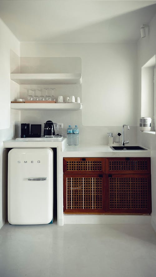 Free Fragment of interior of kitchen with white walls and floor furnished with minimalist shelves and cupboard sink and fridge Stock Photo