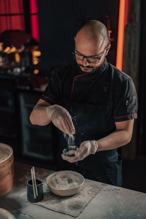 Free A skilled chef in a dark kitchen prepares dumplings, focusing on craftsmanship and culinary art. Stock Photo