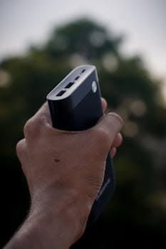 A close-up shot of a hand holding a power bank against a blurred nature background.