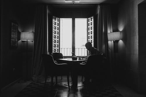 Schattenbildfotografie Des Mannes, Der Auf Stuhl Neben Offenem Fenster Sitzt