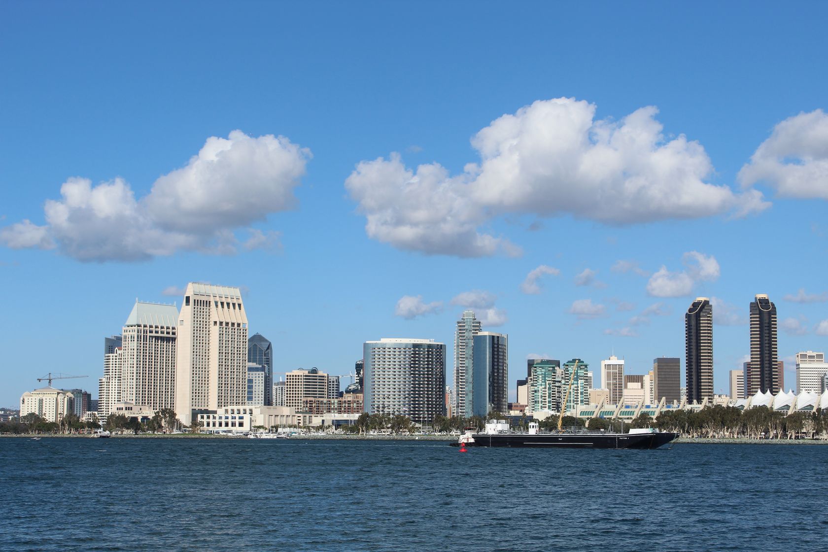 View of San Diego skyline with tall buildings and a ship on a bright day.
