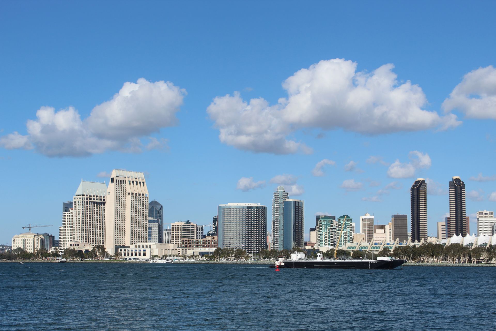 View of San Diego skyline with tall buildings and a ship on a bright day.