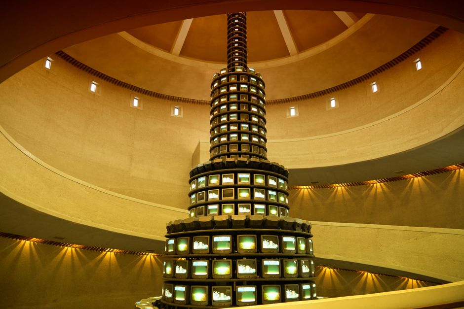 Explore this stunning modern art installation featuring a striking tower of televisions in an architectural space. Explore this stunning modern art installation featuring a striking tower of televisions in an architectural space.