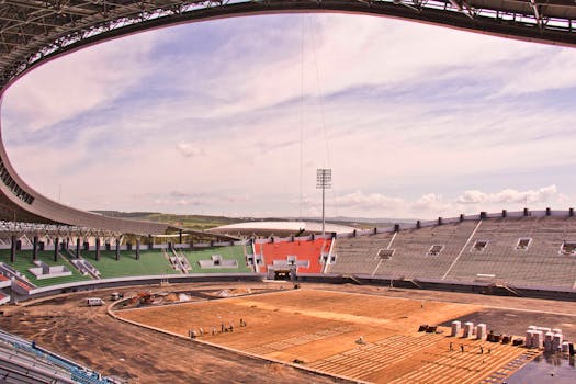 Wide-angle view of a stadium under construction, showcasing seating and a cloudy sky.