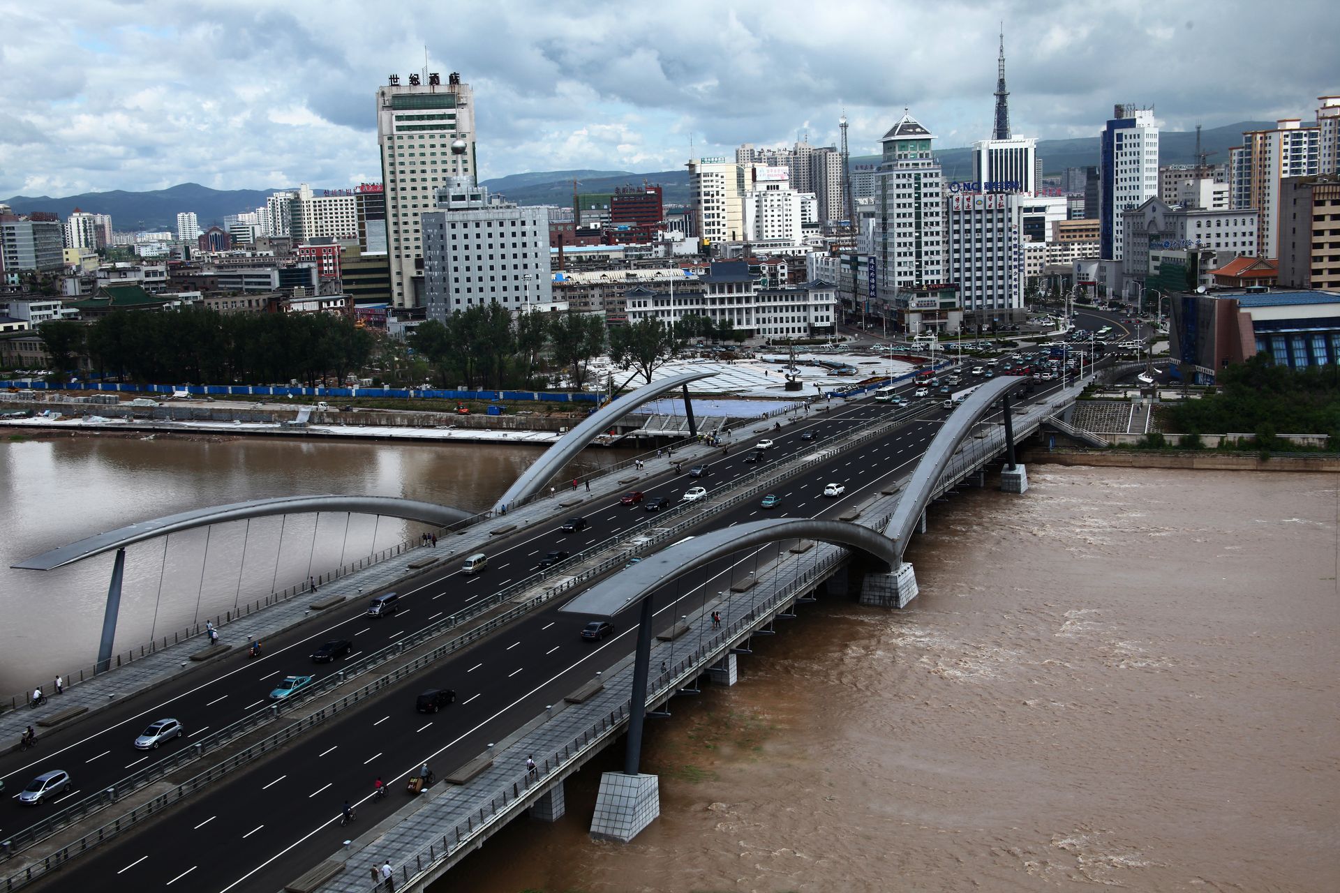 Aerial view of a modern bridge over a river with a city skyline in the background.