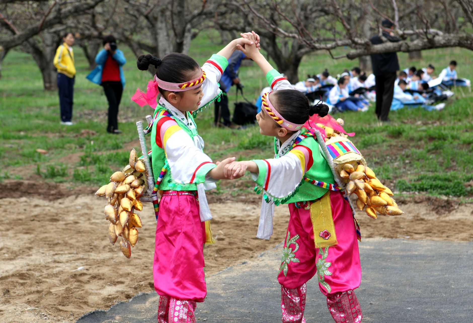 Two children performing a traditional cultural dance in colorful costumes outdoors during a festival.