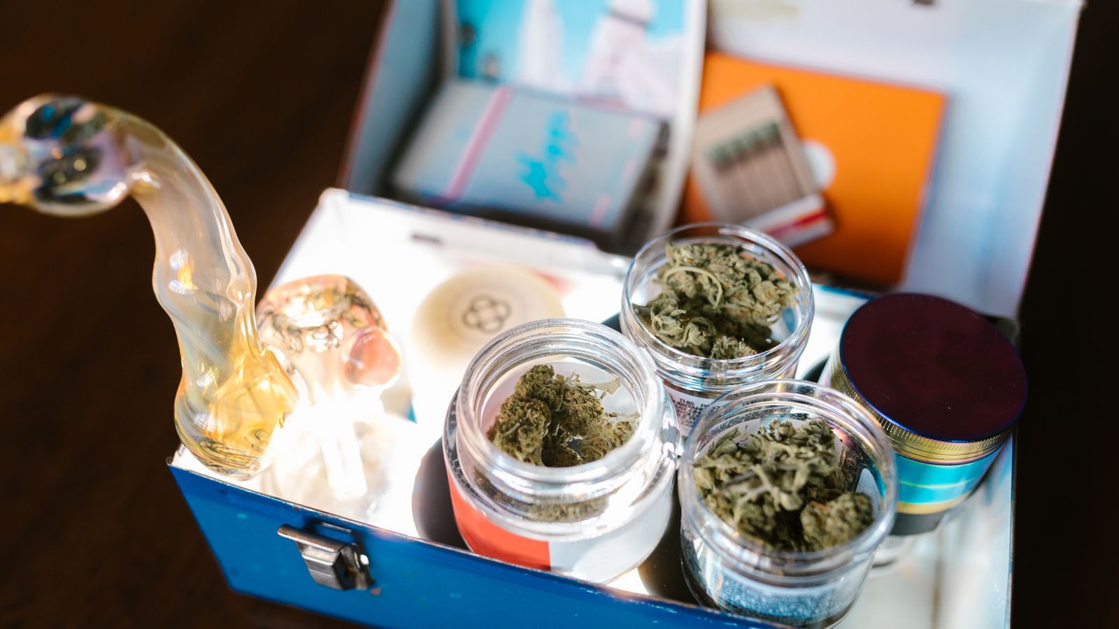 Open cannabis box containing weed, glass pipe, and rolling papers for legal use.