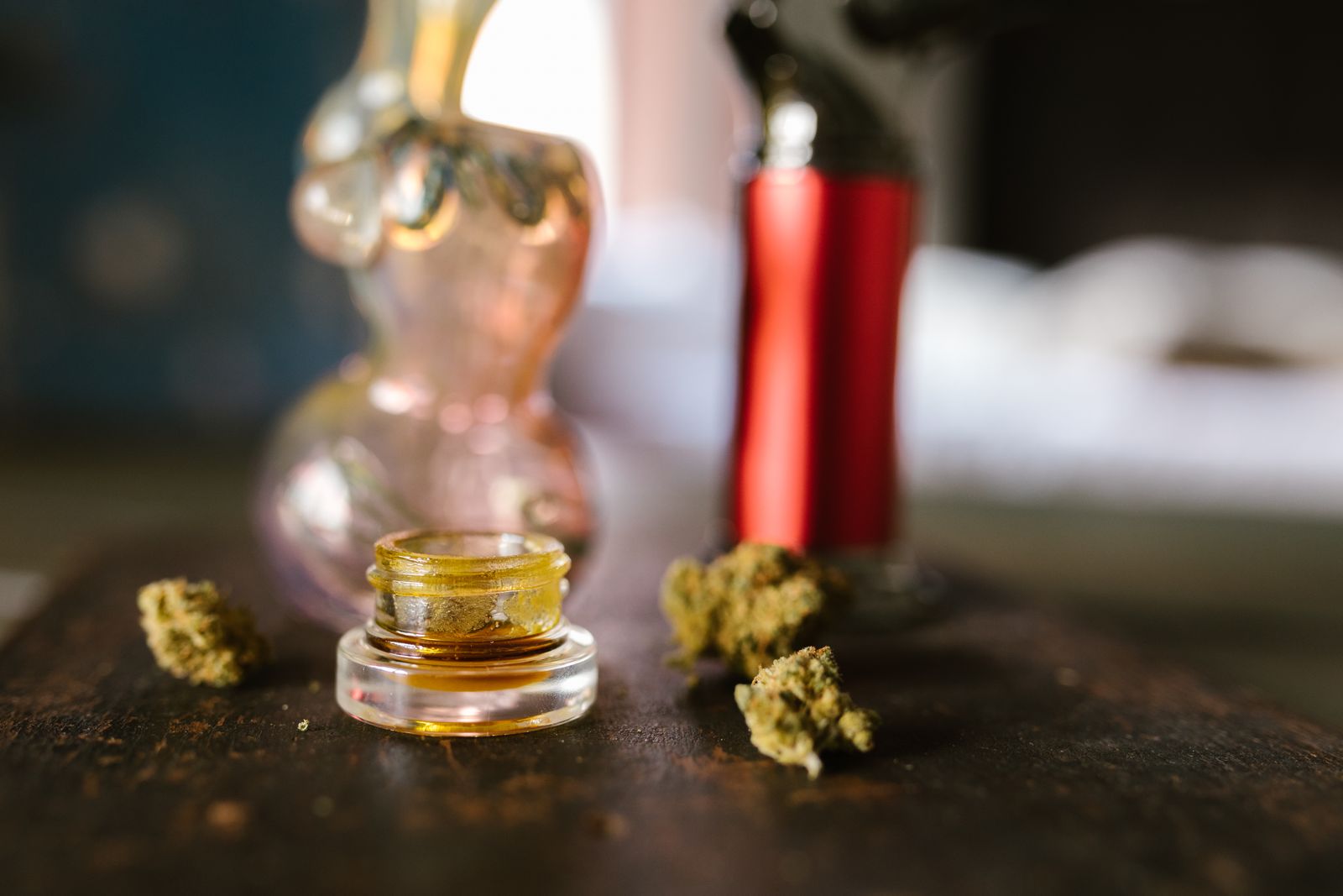 Glass jar of hash rosin surrounded by dried cannabis flower and concentrate tools