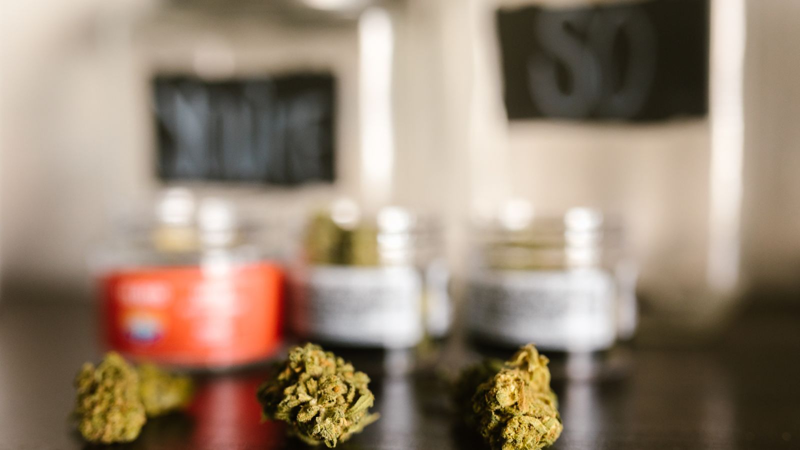 Macro shot of cannabis buds with blurred glass jars in the background, emphasizing texture and color.