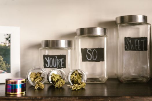 Glass jars filled with cannabis buds artistically arranged on a shelf with playful labels.