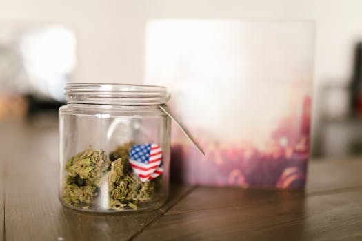 A close-up of a glass jar containing cannabis with an American flag symbol pinned to it, indoors.