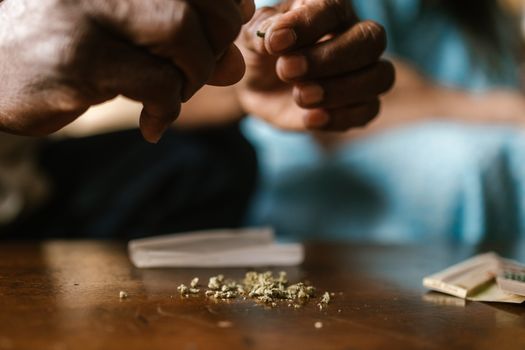 Hands rolling a cannabis joint with marijuana buds and papers on a table.