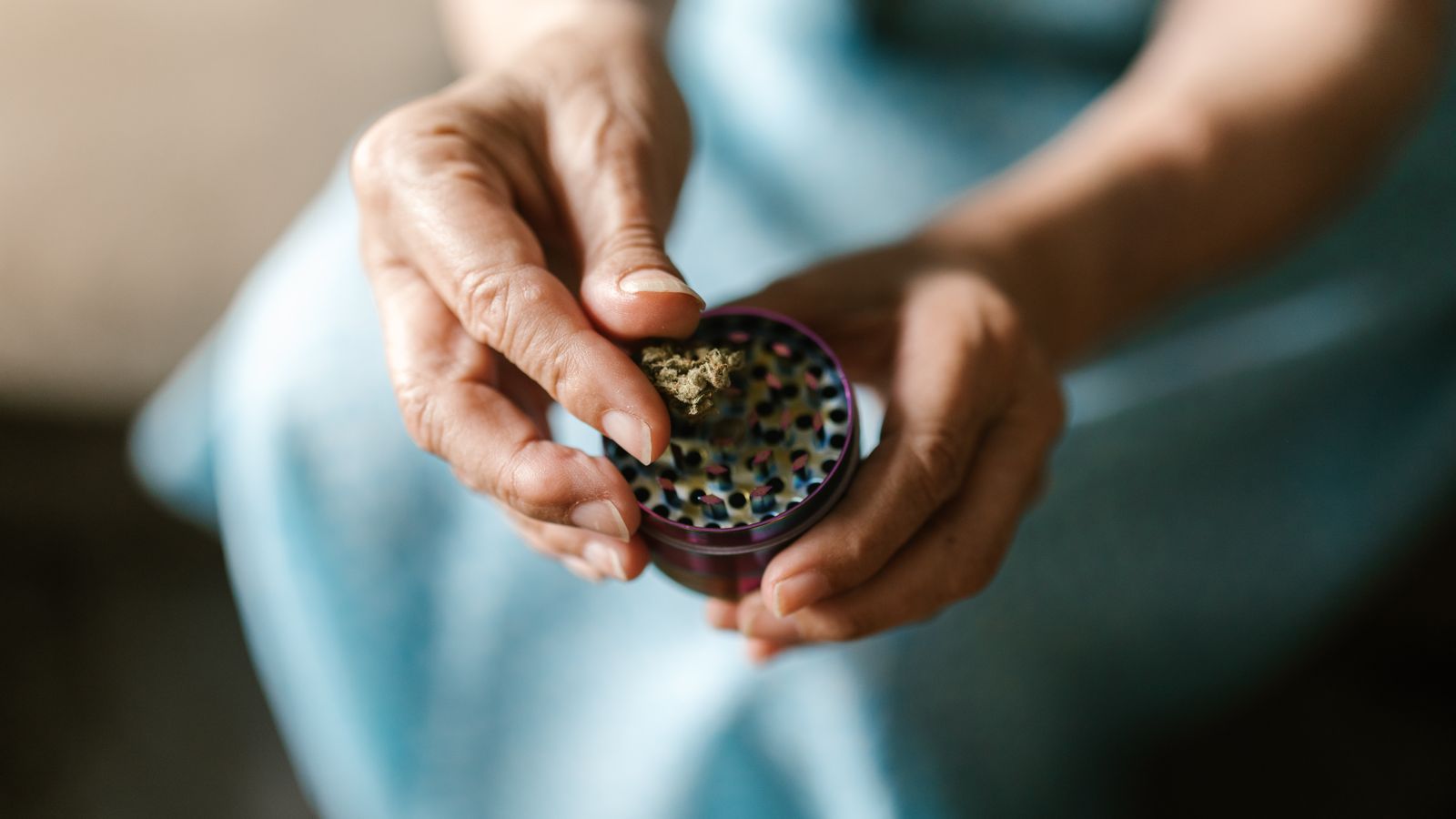 A close-up image showing hands using a weed grinder with cannabis.