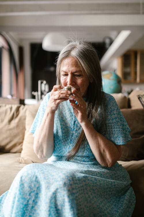 Elderly Woman Sitting on Sofa while Smelling Weed 
