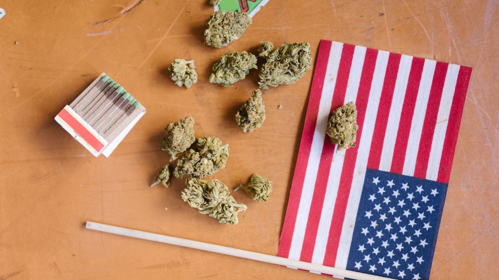 Top view of cannabis buds, matchsticks, and American flag on a wooden table.