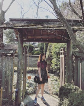 阳光明媚的日子里，一位穿着时尚连衣裙的年轻女子站在日本传统花园的入口处