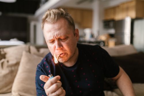 Free A man skillfully lights a cigarette with a lighter in a cozy indoor setting, exuding a casual vibe. Stock Photo