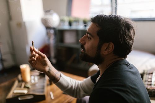 Free A man sitting indoors holding a cannabis joint, relaxed and thoughtful. Stock Photo