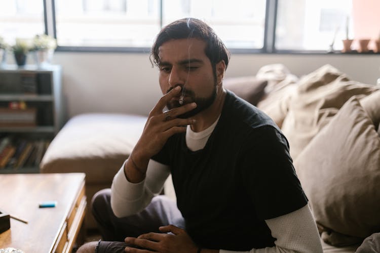 A Bearded Man Sitting On The Couch While Smoking Weed