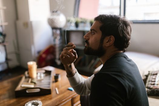 A man is seated in a cozy room, enjoying a relaxed moment smoking indoors.