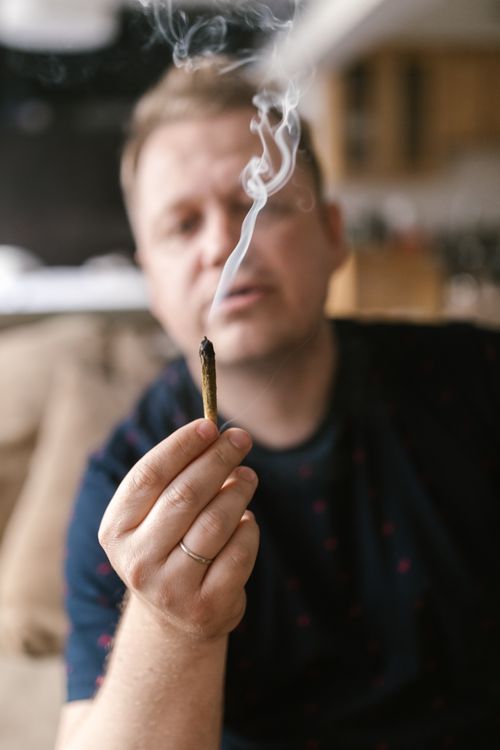 Free Close-up of a man holding a marijuana joint in a living room setting. Stock Photo