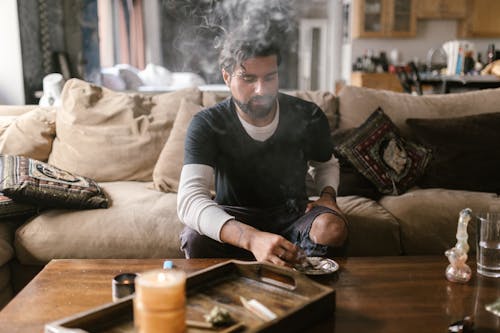 Free Man in Black and White Long Sleeve Shirt Sitting on Couch Smoking Marijuana Stock Photo