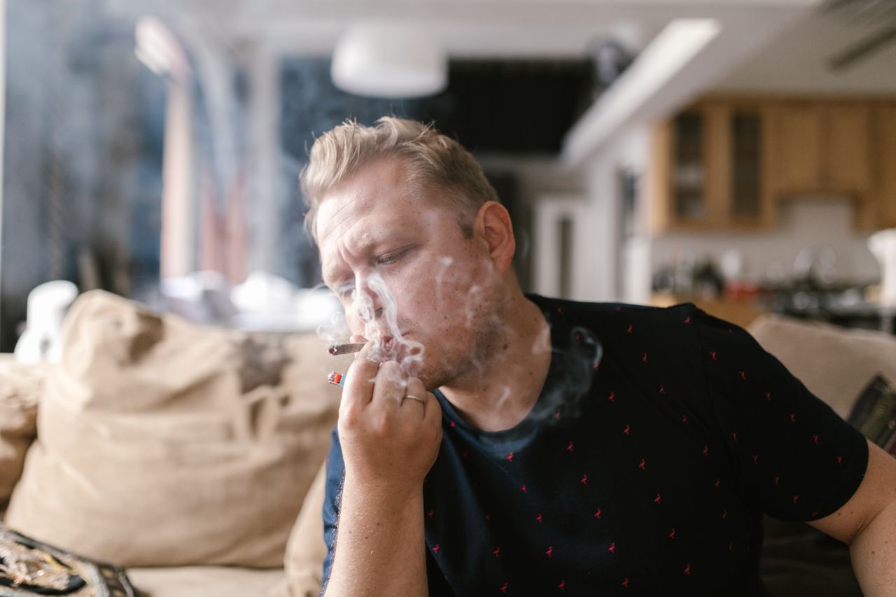 adult man enjoying a smoke indoors surrounded by a casual home setting