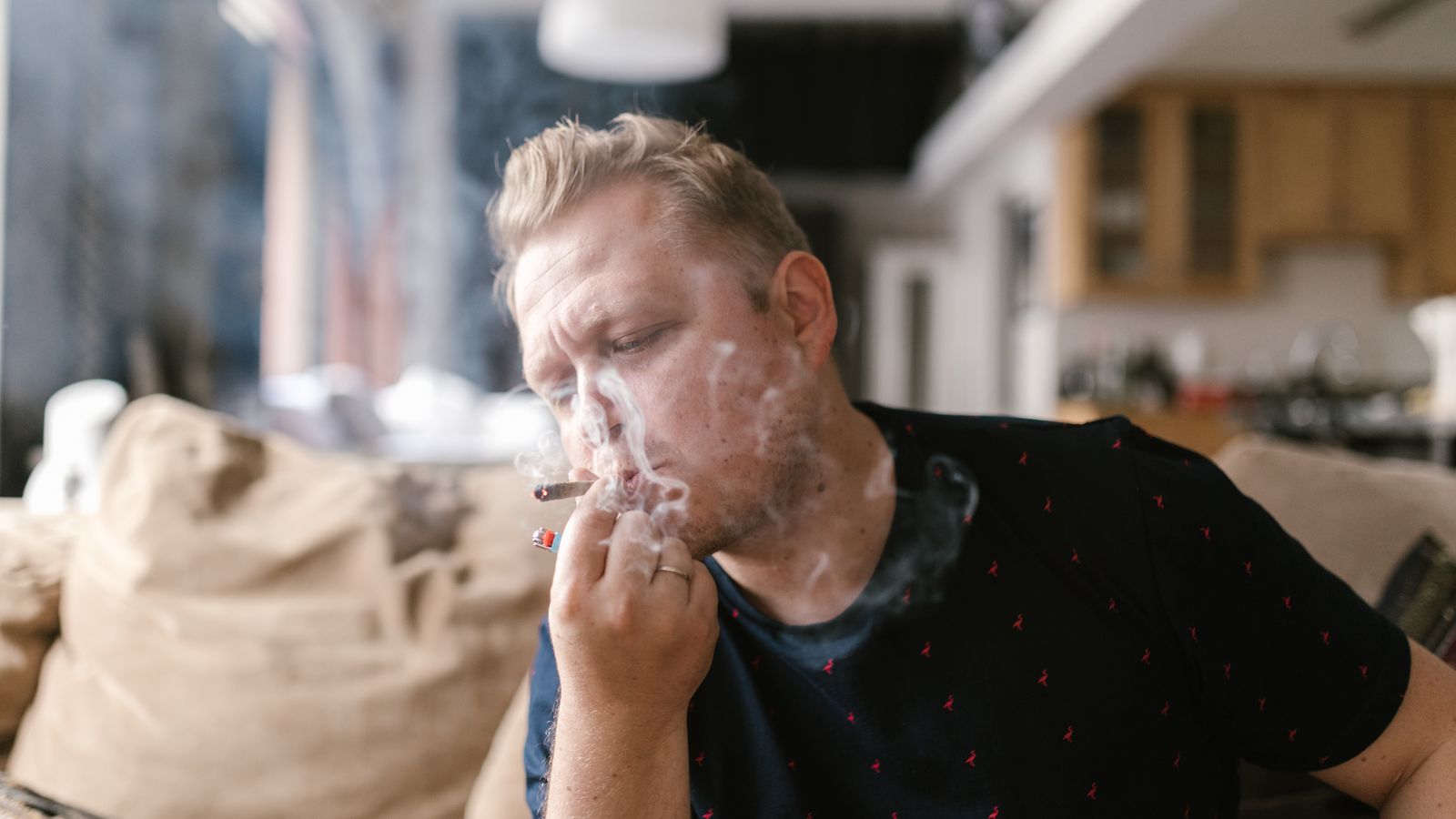 Adult man enjoying a smoke indoors, surrounded by a casual home setting.