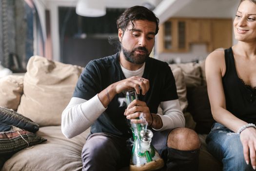 A couple enjoying a relaxed moment indoors with a bong, emphasizing leisure and companionship.