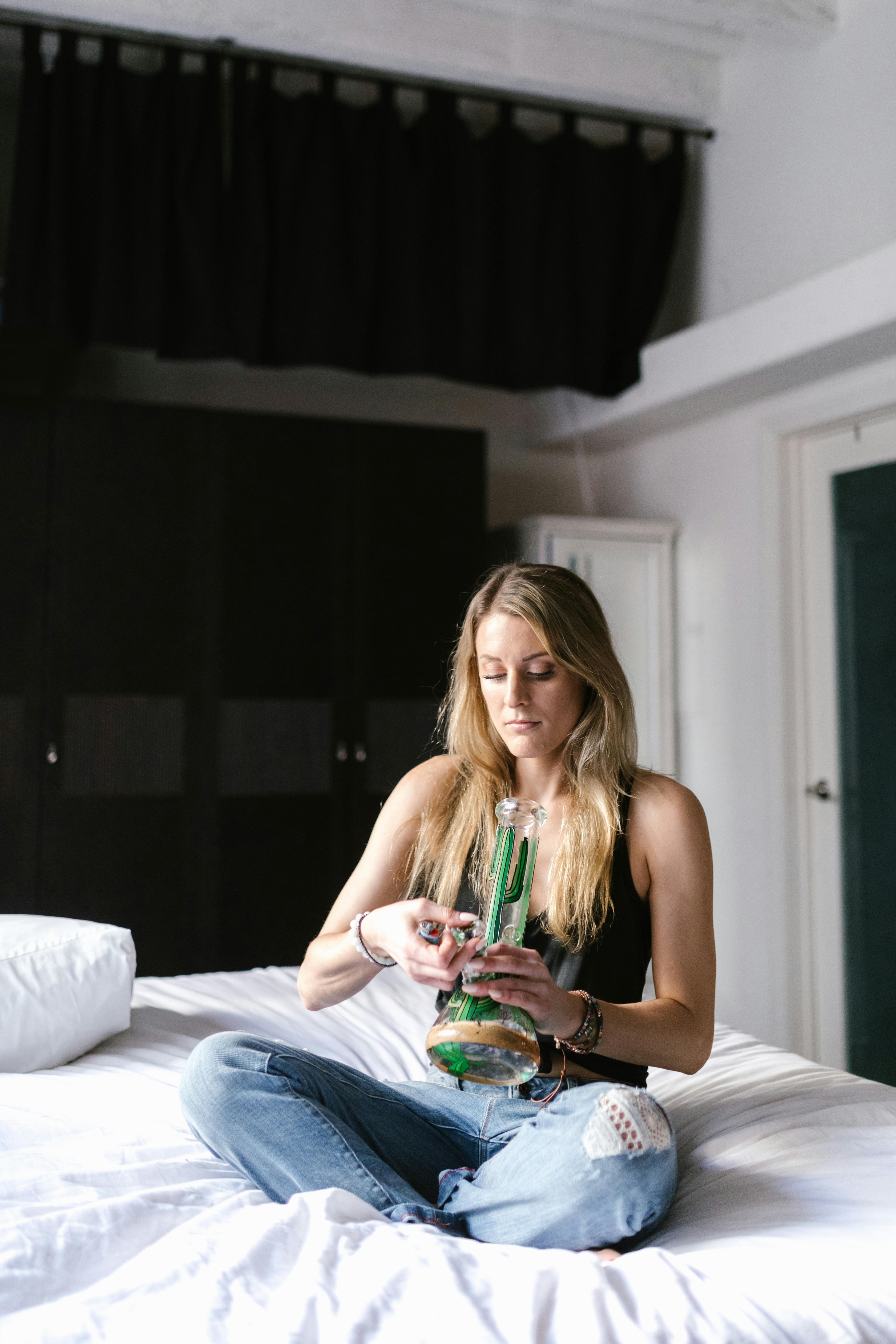 woman sitting on bed holding clear glass bottle