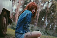 一名红发女子身穿牛仔服，在森林中靠近一辆车