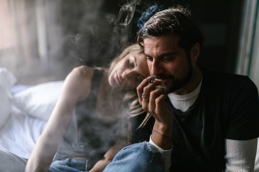 Two adults sitting together indoors, relaxing and smoking, creating a smoky ambiance.