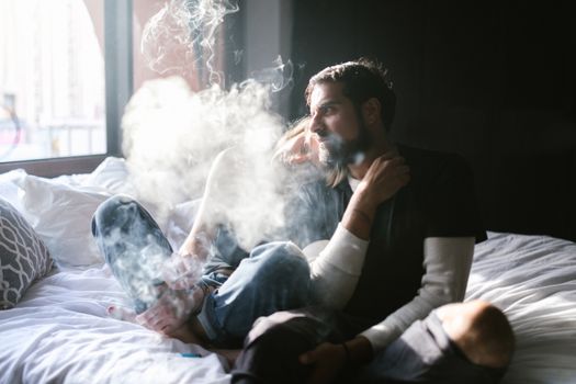 A Man in Black Shirt Sitting on the Bed while Smoking Weed