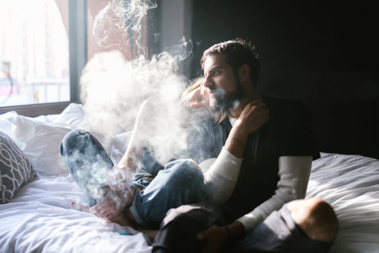 A Man In Black Shirt Sitting On The Bed While Smoking Weed