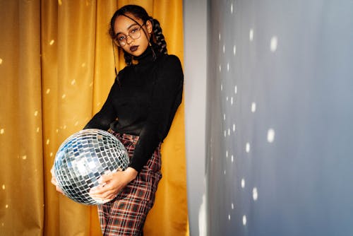 Free A Woman in Black Turtleneck Sweater and Plaid Skirt Holding a Disco Ball Stock Photo