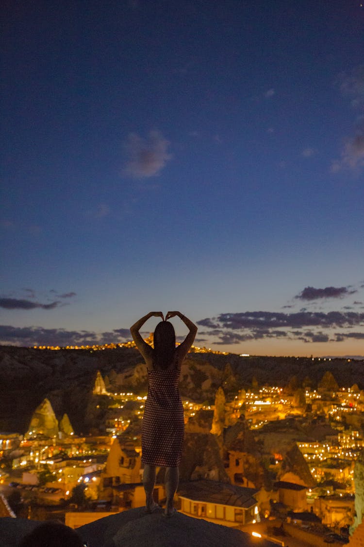 Silhouette Of A Woman In A Balancing Pose Against Illuminated Townscape At Dusk