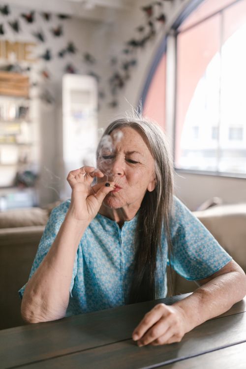 Free Senior woman smoking indoors, embracing leisure time. Natural light and soft colors create a relaxed atmosphere. Stock Photo