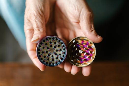 A detailed close-up of hands holding an open weed grinder against a blurred background.