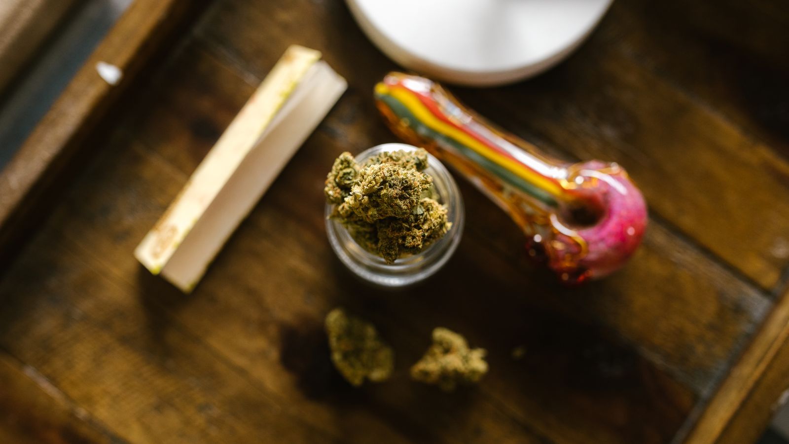 Top view of cannabis buds, a glass pipe, and rolling papers on a wooden surface.