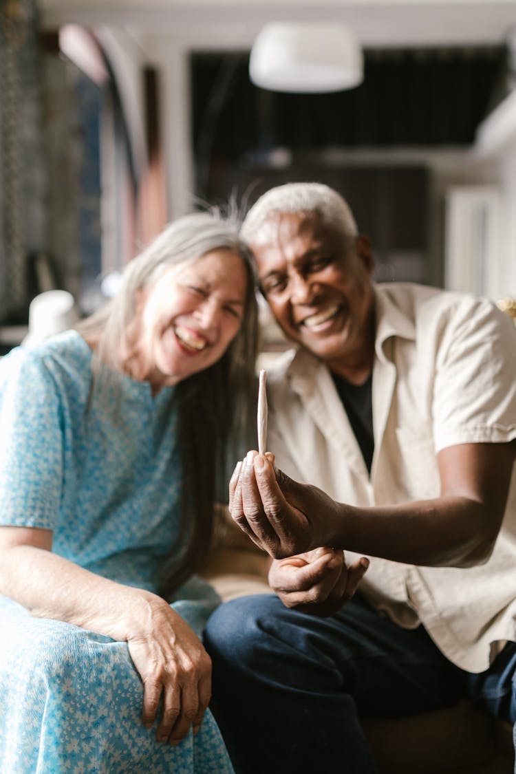 An Elderly Couple Sitting In The Living Room Holding A Cigarette