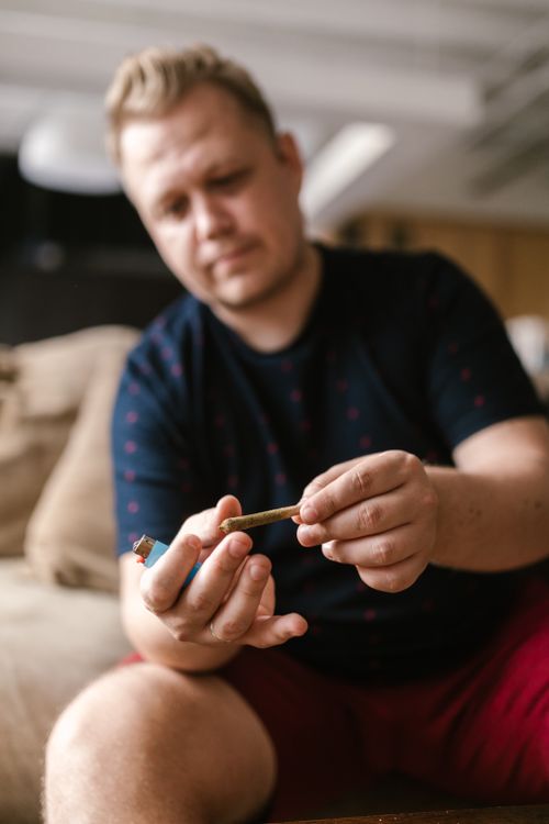 Free Man seated indoors holding a cannabis joint, emphasizing casual lifestyle. Stock Photo