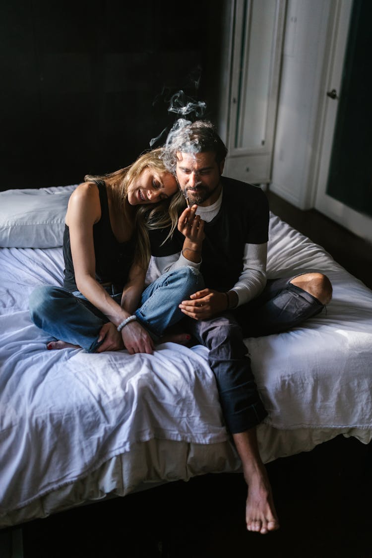 Couple Sitting On The Bed While Smoking Marijuana