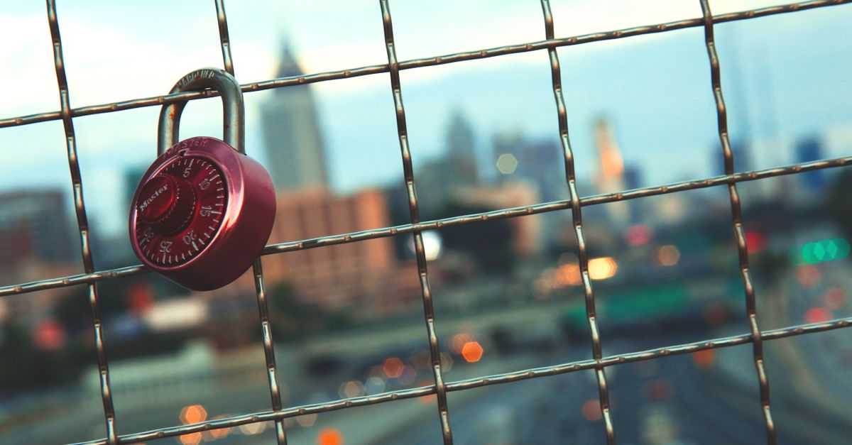 A red padlock on a wire fence with a blurred view of Atlanta's skyline during the day.