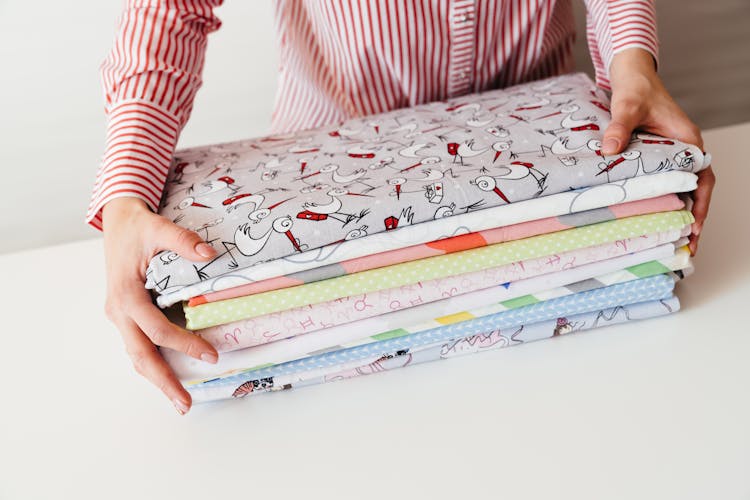 Person In Red And White Striped Long Sleeve Shirt Holding Pile Of Printed Fabrics