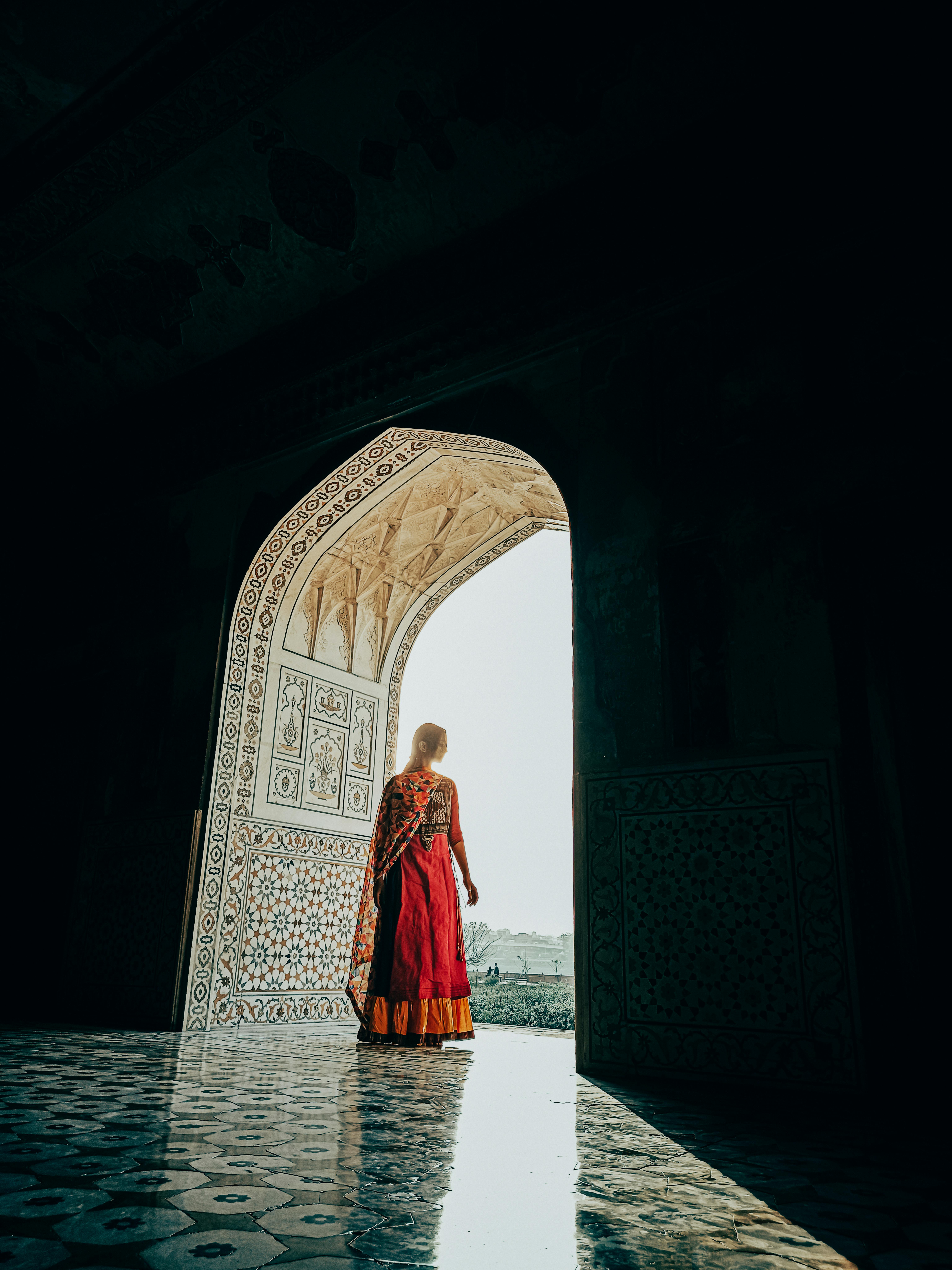 A woman in a traditional saree stands in a grand, ornate doorway with intricate patterns.