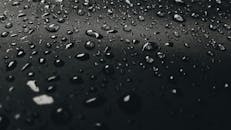 特写镜头捕捉了黑暗纹理表面上的水滴，营造出一种阴郁而抽象的氛围