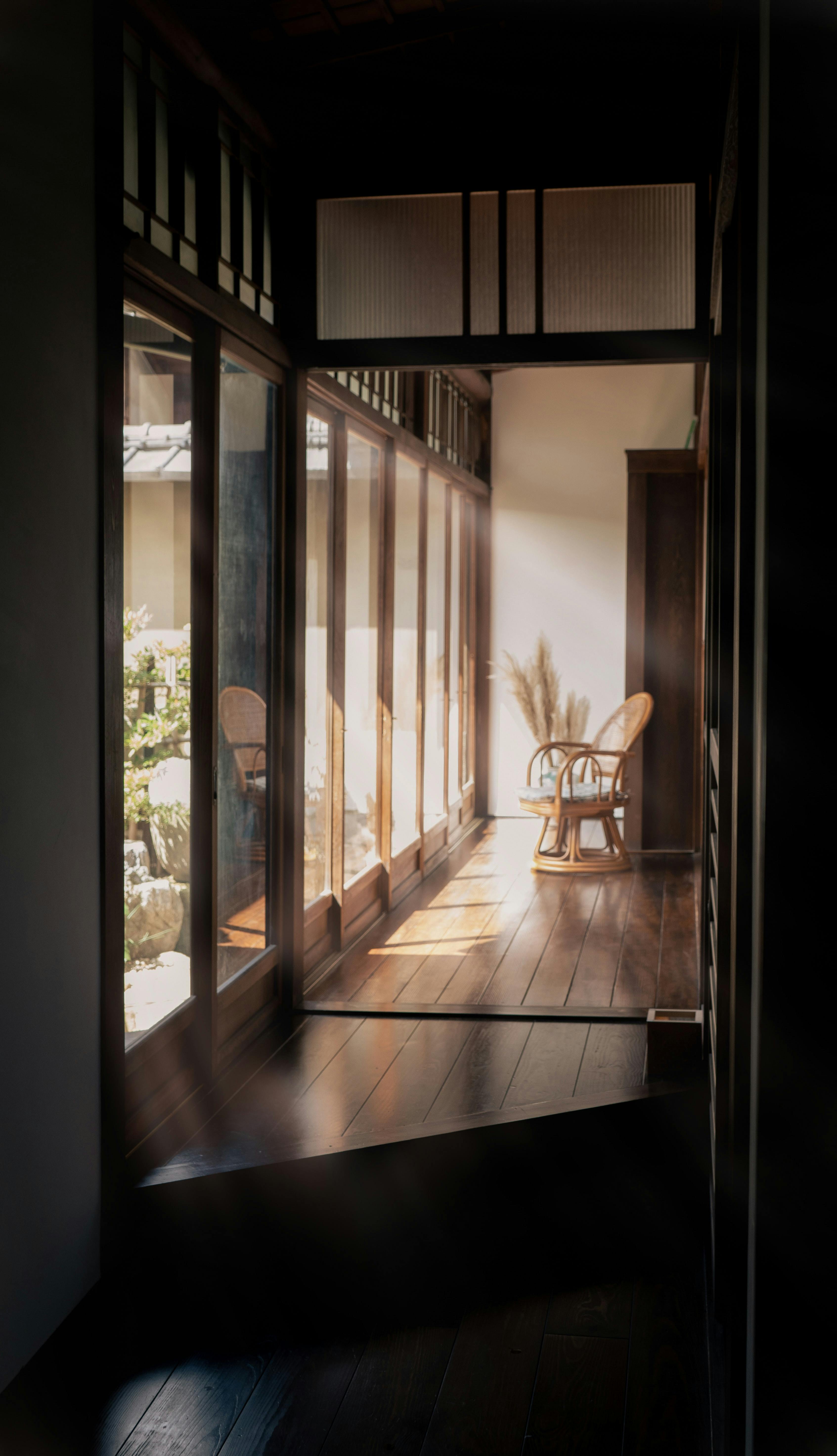 A serene sunlit hallway in a traditional Japanese home with wooden floors and large windows.