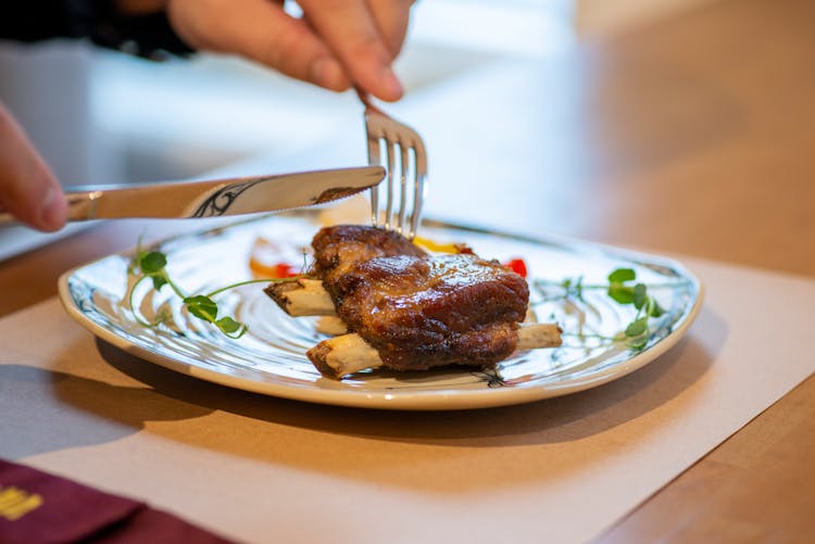 Close-up Of Person Eating Meat With Knife And Fork