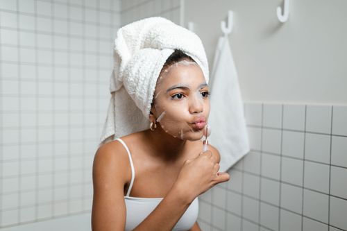 Free A young woman with a towel turban applies a facial mask, enjoying her skincare routine in a modern bathroom. Stock Photo